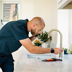 Bristan engineer repairing a brushed brass kitchen tap in a customer's home